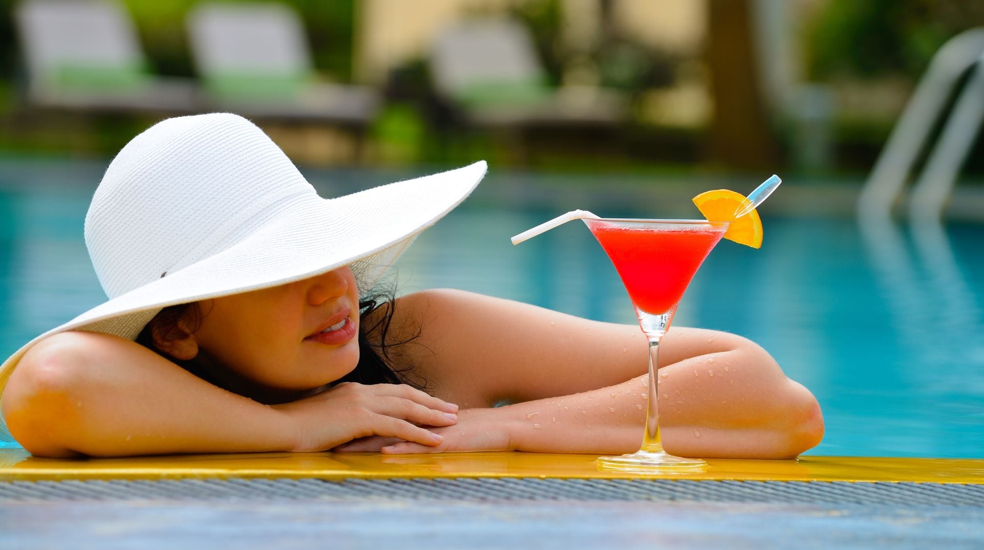 Girl With A Cocktail At The Edge Of The Swimming Pool . Red Cocktail With An Orange Slice.