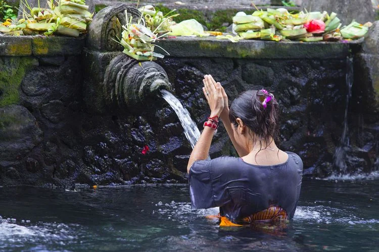 Woman praying in water in front of a wall fountain